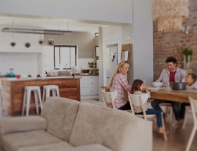 Familie sitzt gemeinsam beim Essen an einem Tisch in ihrem offenen Küche-Wohnbereich
