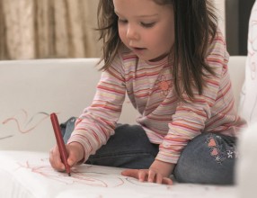 Ein Kleinkind bemalt mit einem Filzstift eine weiße Couch – Symbolbild für eine Privathaftpflichtversicherung
